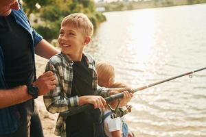 positivo emozioni. padre e madre con figlio e figlia su pesca insieme all'aperto a estate foto