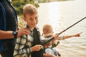 apprendimento per pesca. padre e madre con figlio e figlia insieme all'aperto a estate foto