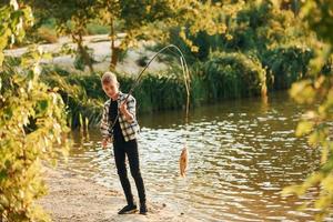 con bene presa. ragazzo nel casuale Abiti nel su pesca all'aperto a estate foto