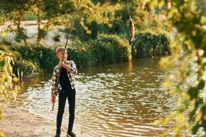 con bene presa. ragazzo nel casuale Abiti nel su pesca all'aperto a estate foto