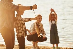 nel casuale Abiti. padre e madre con figlio e figlia su pesca insieme all'aperto a estate foto