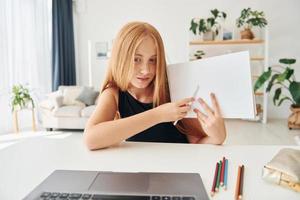 in linea formazione scolastica. femmina adolescente con bionda capelli è a casa a giorno foto