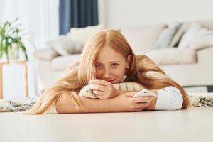 con smartphone nel mani. femmina adolescente con bionda capelli è a casa a giorno foto