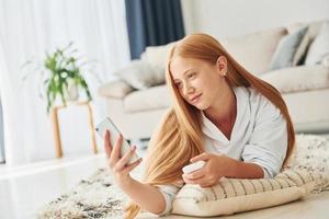 con smartphone nel mani. femmina adolescente con bionda capelli è a casa a giorno foto