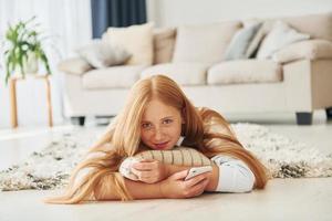 con smartphone nel mani. femmina adolescente con bionda capelli è a casa a giorno foto