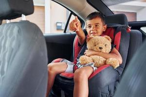 poco ragazzo con orsacchiotto orso è seduta nel il automobile foto