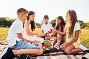 comunicare con ogni Altro. gruppo di contento bambini è all'aperto su il allegro campo a giorno foto