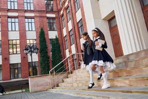 concezione di formazione scolastica. Due studentesse è al di fuori insieme vicino scuola edificio foto