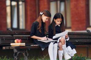Due studentesse è seduta al di fuori insieme vicino scuola edificio foto
