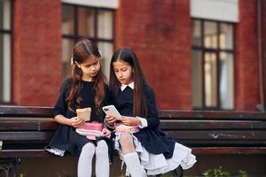 Due studentesse è seduta al di fuori insieme vicino scuola edificio foto