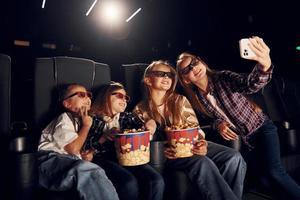 moderno tecnologie. gruppo di bambini seduta nel cinema e Guardando film insieme foto