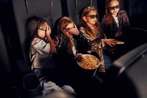 avendo divertimento. gruppo di bambini seduta nel cinema e Guardando film insieme foto