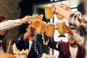 applauso insieme. gruppo di giovane amici seduta nel bar con birra foto