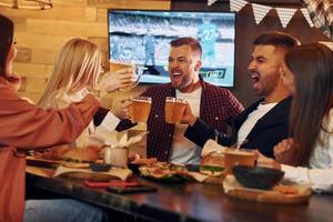 contro tv. gruppo di giovane amici seduta insieme nel bar con birra foto