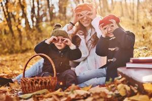 seduta su il terra. madre con sua poco figlio e figlia è avendo divertimento nel il autunno parco foto