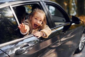 poco ragazza seduta nel il nero automobile e guardare attraverso il finestra foto