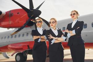 tre hostess. equipaggio di aeroporto e aereo lavoratori nel formale Abiti in piedi all'aperto insieme foto