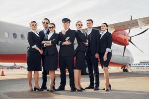 in posa per un' telecamera. equipaggio di aeroporto e aereo lavoratori nel formale Abiti in piedi all'aperto insieme foto