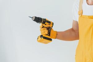 tuttofare nel giallo uniforme in piedi contro bianca parete con automatico Cacciavite. Casa rinnovamento concezione foto