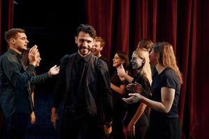 dando alto cinque, festeggiare successo. gruppo di attori nel buio colorato Abiti su prova nel il Teatro foto