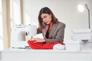 sarta lavori con rosso stoffa. giovane donna nel formale Abiti è al chiuso. concezione di stile foto