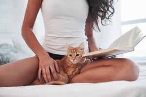 particella Visualizza. attraente bionda riposo su il bianca letto con sua carino gattino foto