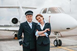 uomo con donna. aereo equipaggio nel opera uniforme è insieme all'aperto vicino aereo foto