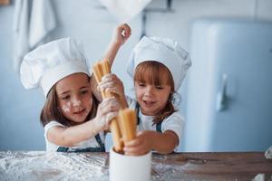 avendo divertimento con spaghetti. famiglia bambini nel bianca capocuoco uniforme preparazione cibo su il cucina foto