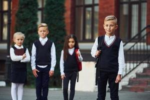 gruppo di bambini nel scuola uniforme in posa per il telecamera all'aperto insieme vicino formazione scolastica edificio foto