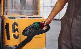 giovane maschio lavoratore nel uniforme è nel il magazzino spingendo pallet camion foto