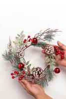 donna mani siamo Tenere fatto a mano riutilizzabile Natale ghirlanda fatto di albero rami, rosso frutti di bosco, coni su bianca sfondo. foto