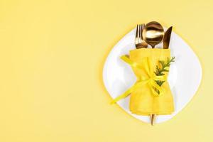 natale tavolo ambientazione con d'oro posate impostato decorato con arborvitae ramoscello su bianca piatto su giallo. foto
