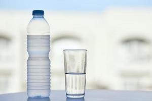 bottiglia di acqua e bicchiere di acqua su tavolo nel caldo estate giorno, avvicinamento foto