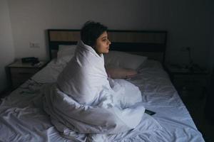 giovane donna avvolto nel un' coperta fissando in il distanza foto