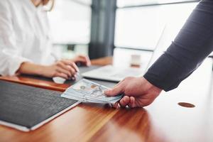 vicino su Visualizza di dell'uomo mani con i soldi in casa contro donna quello lavori di il computer portatile foto