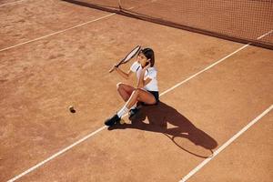 seduta su il terra. femmina tennis giocatore è su il Tribunale a giorno foto