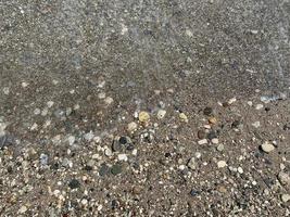 sfondo di bianca mare ciottoli su il spiaggia. selettivo messa a fuoco, sfocato mare onde su sfondo. mare ghiaia struttura sfondo. oceano spiaggia vacanza concetto foto