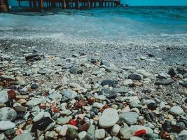 vacanza di il mare su il spiaggia. ciottolo spiaggia con pietre. bagnato, piccolo, multicolore pietre vicino il acqua, onde con bianca schiuma foto