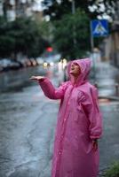 giovane sorridente donna con impermeabile mentre godendo un' piovoso giorno. foto