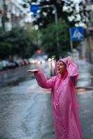 giovane sorridente donna con impermeabile mentre godendo un' piovoso giorno. foto