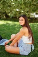 giovane ragazza lavori con un' computer portatile, seduta su il prato. foto