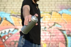 giovane graffiti artista obiettivi il suo spray può su sfondo di colorato graffiti nel rosa toni su mattone parete. strada arte e contemporaneo pittura processi foto