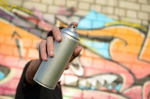 giovane graffiti artista obiettivi il suo spray può su sfondo di colorato graffiti nel rosa toni su mattone parete. strada arte e contemporaneo pittura processi foto