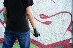 un' giovane teppista con un' spray può sta contro un' calcestruzzo parete con graffiti quadri. illegale vandalismo concetto. strada arte foto