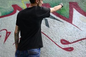 un' giovane teppista vernici graffiti su un' calcestruzzo parete. illegale vandalismo concetto. strada arte foto