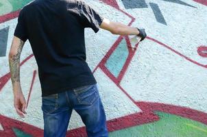 un' giovane teppista vernici graffiti su un' calcestruzzo parete. illegale vandalismo concetto. strada arte foto