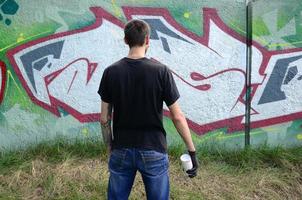 un' giovane teppista con un' spray può sta contro un' calcestruzzo parete con graffiti quadri. illegale vandalismo concetto. strada arte foto