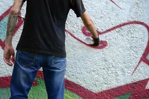 un' giovane teppista vernici graffiti su un' calcestruzzo parete. illegale vandalismo concetto. strada arte foto