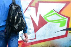 un' giovane graffiti artista con un' nero Borsa sembra a il parete con il suo graffiti su un' parete. strada arte concetto foto