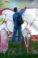 un' pochi Usato dipingere lattine contro il sfondo di il spazio con il parete su quale il giovane tipo disegna un' grande graffiti disegno. moderno arte di disegno muri nel graffiti foto